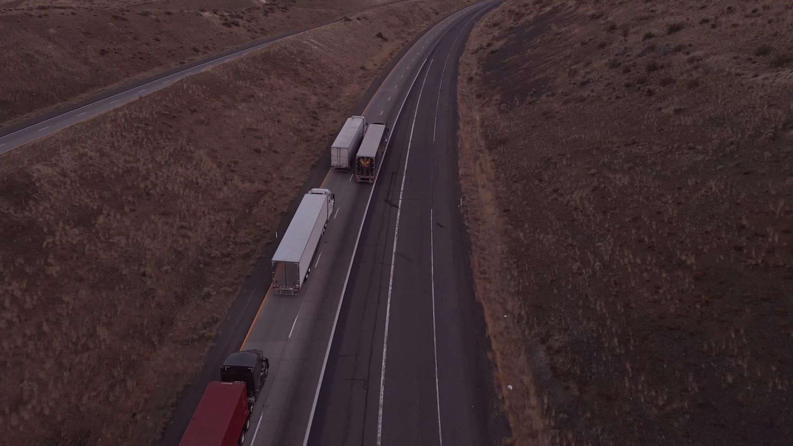 Tractocamiones en una carretera al atardecer, vistos desde arriba